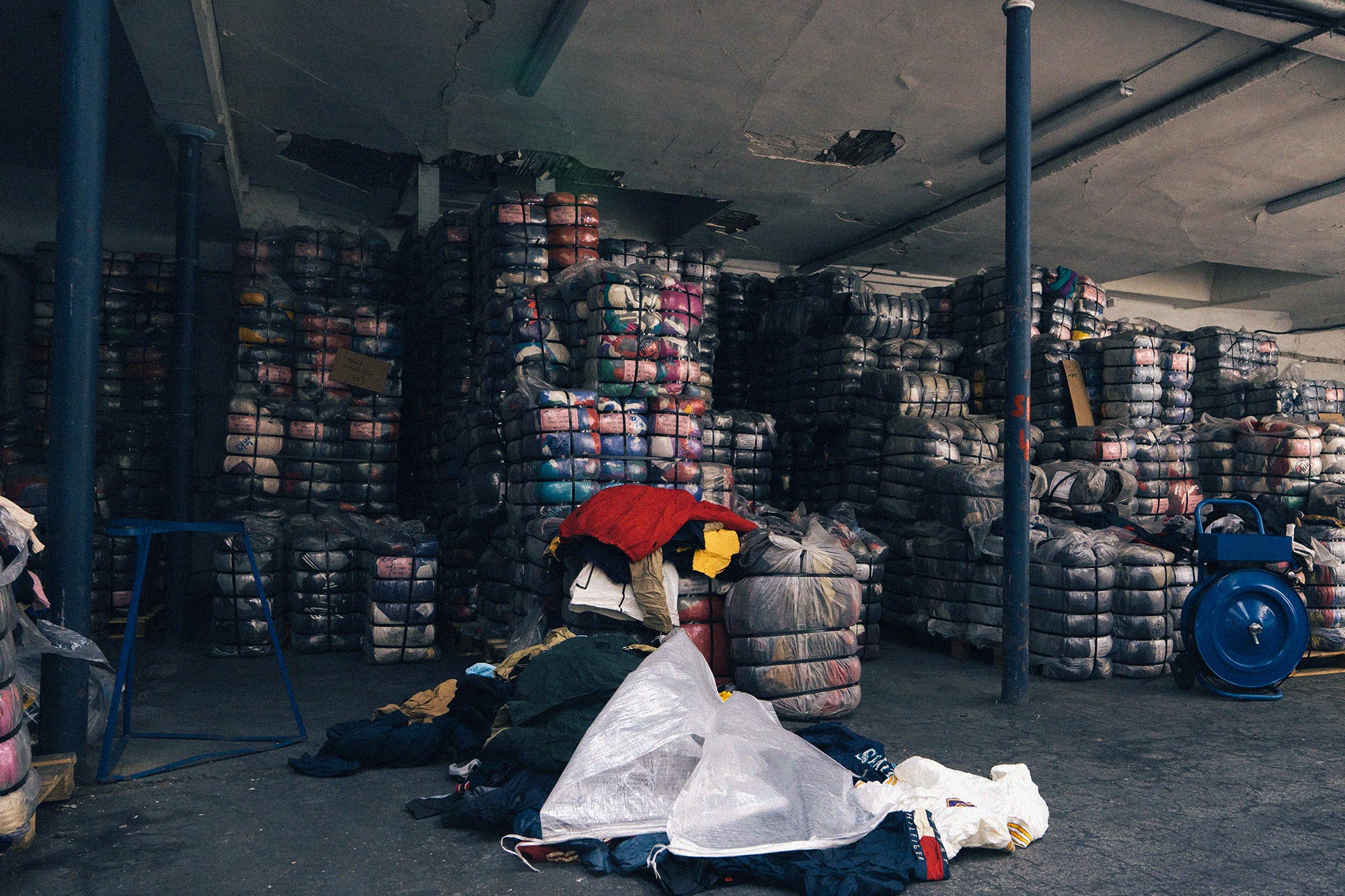 Entrepôt de grossiste en vêtements de seconde main avec balles de fripes empilées et stock textile prêt à l’export et à la revente.